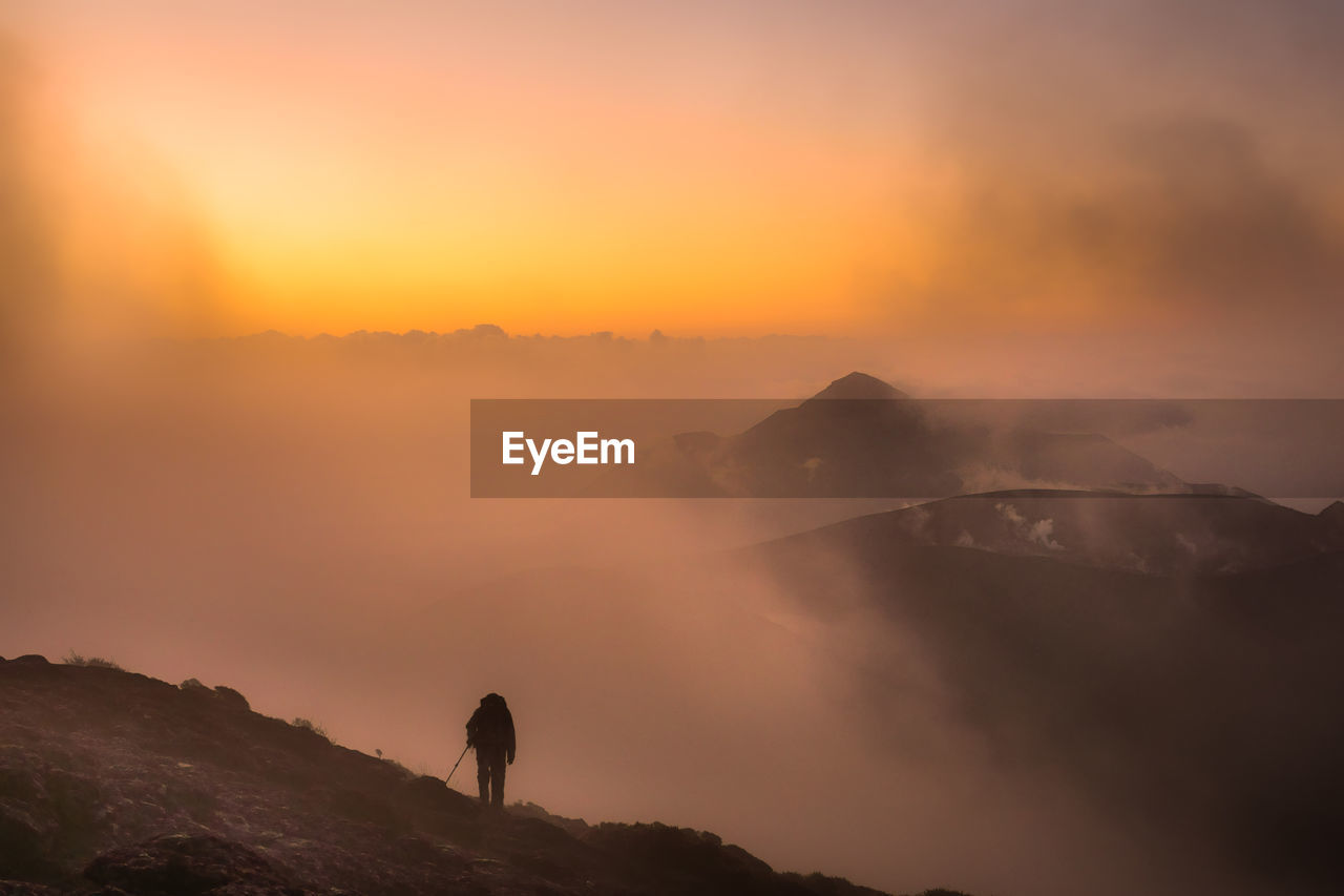 Rear view of silhouette man standing on mountain against sky during sunset