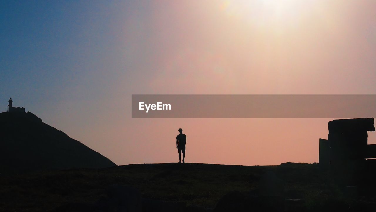 SILHOUETTE MAN STANDING ON ROCK AGAINST SKY DURING SUNSET