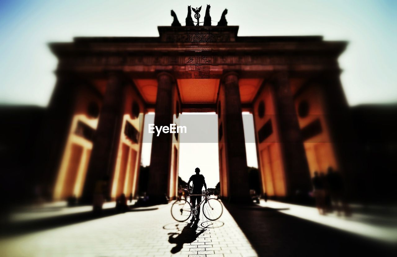 Low angle view of man standing with bicycle in front of brandenburg gate