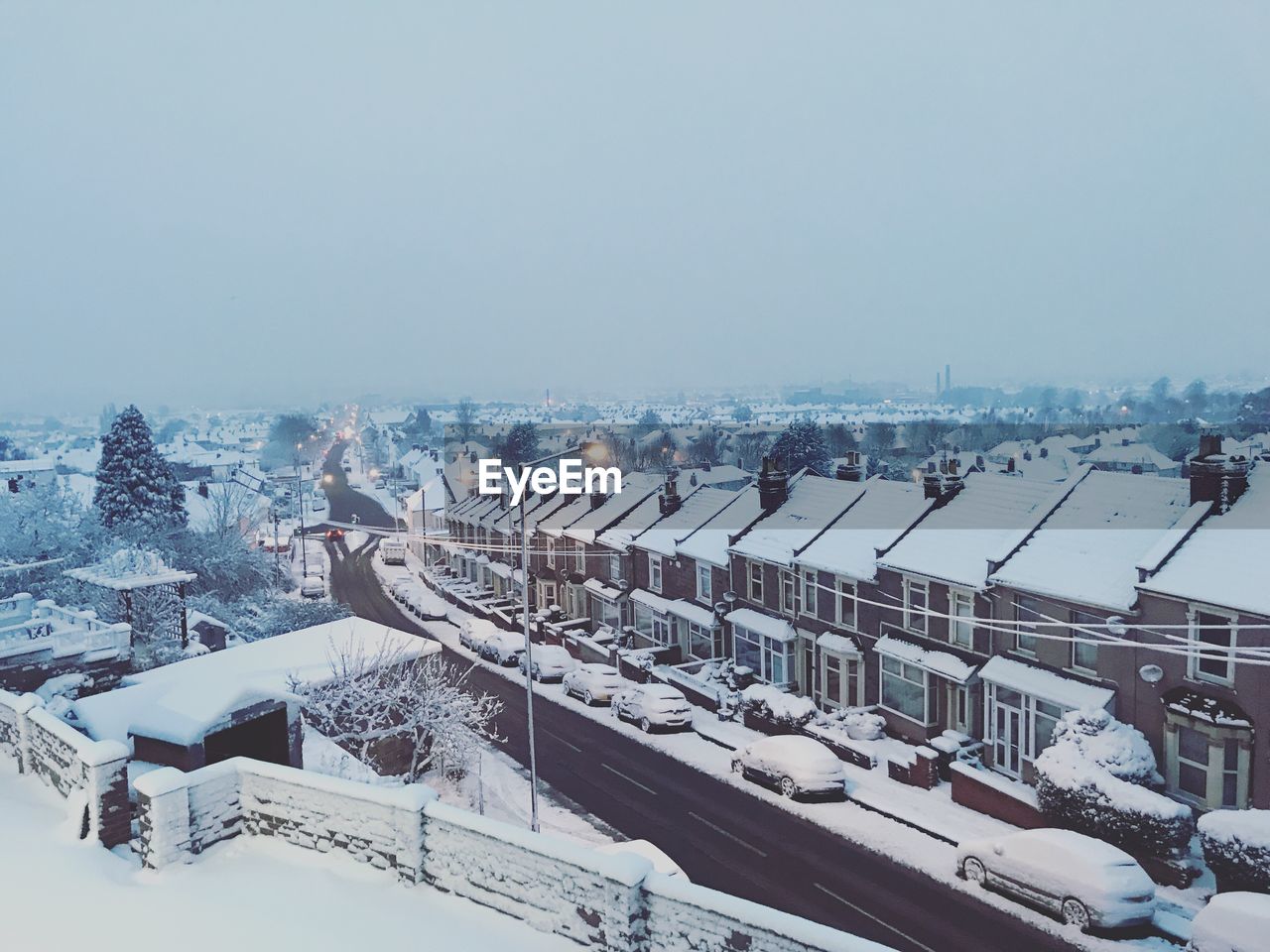 HIGH ANGLE VIEW OF SNOW COVERED HOUSES BY CITY AGAINST SKY