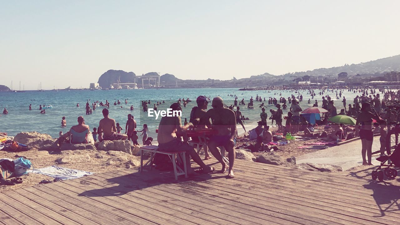 PEOPLE RELAXING AT BEACH AGAINST SKY