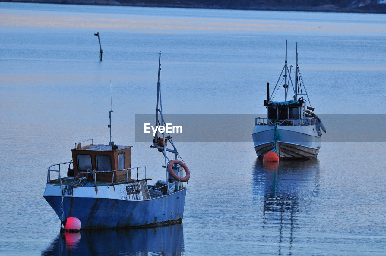 Fishing boats sailing in sea during sunset