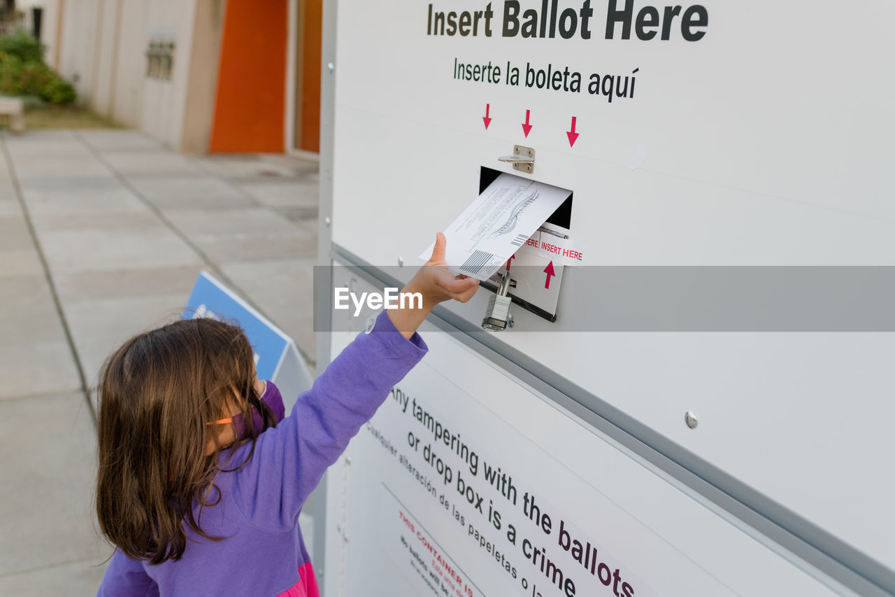 Little girl placing ballot in a drop box for absentee voting