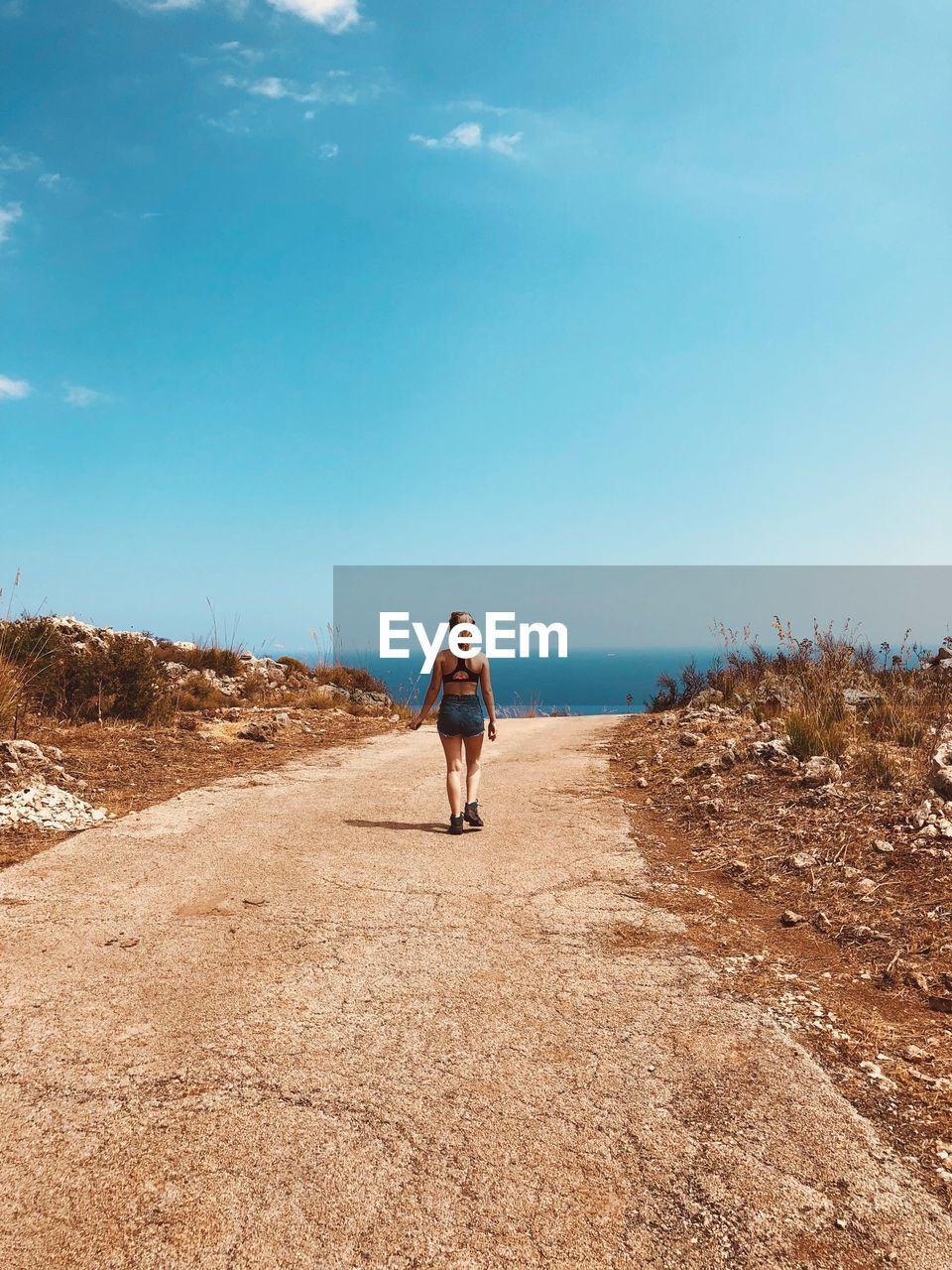 Rear view of teenage girl walking on footpath against blue sky