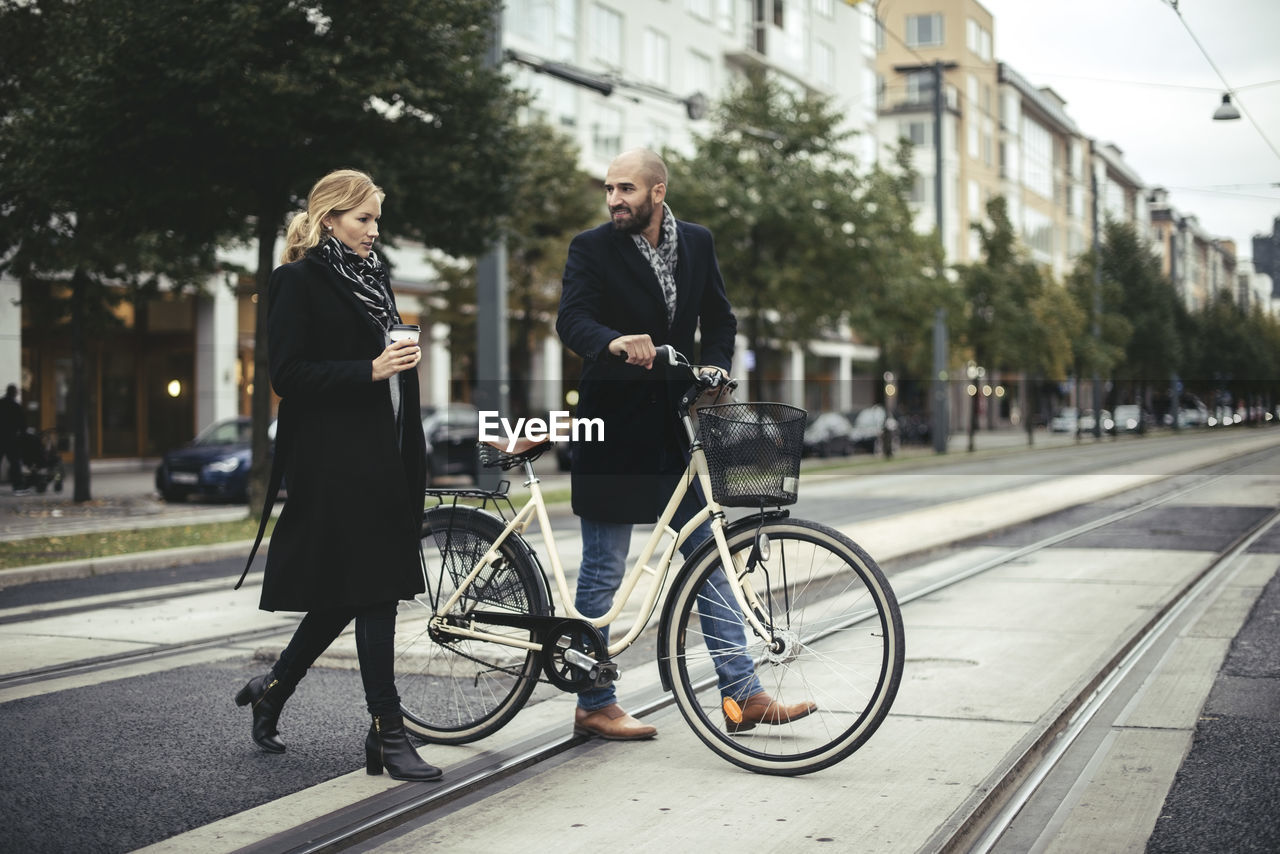 Full length of business people with bicycle crossing city street