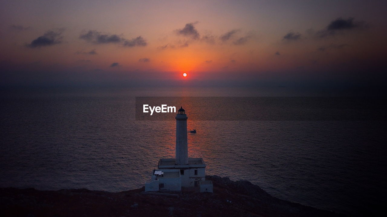 Lighthouse by sea against sky during sunset