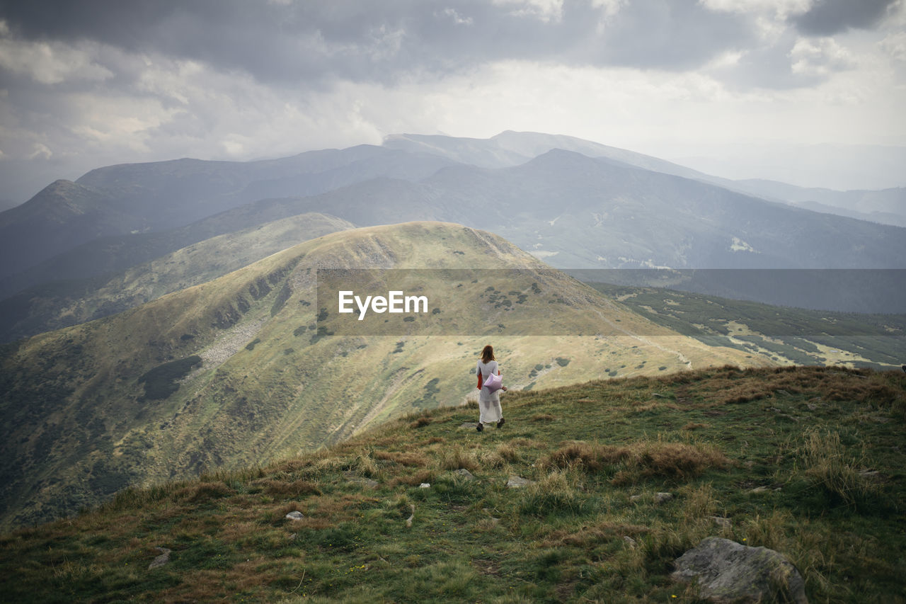 Rear view of woman walking on mountain against cloudy sky