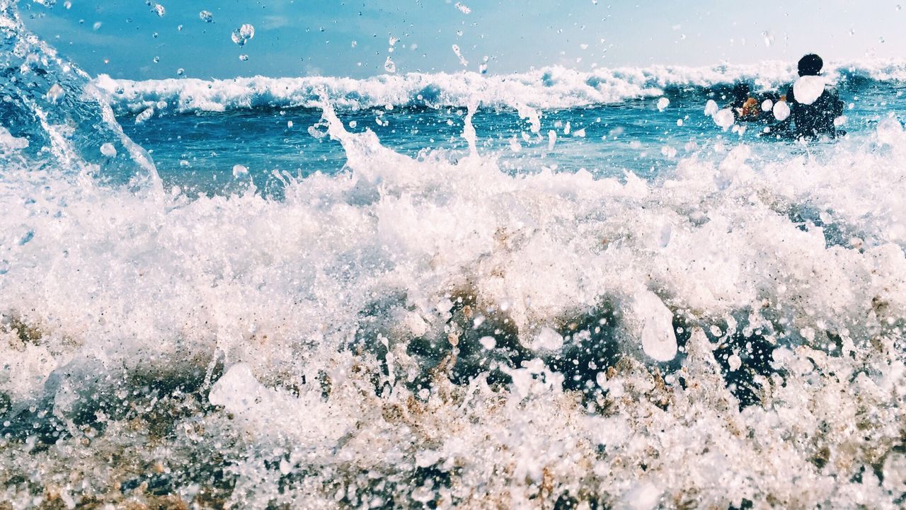 Sea waves splashing at beach against sky