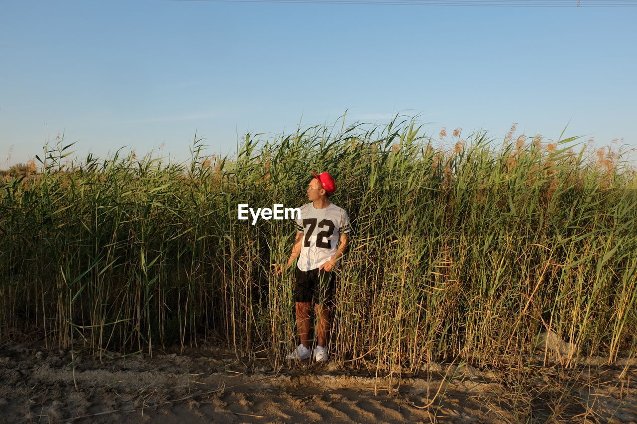 Young man standing against plants on field