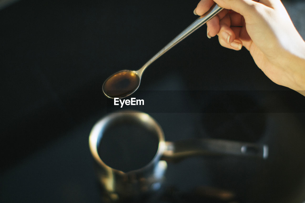 Cropped image of hand holding spoon over container