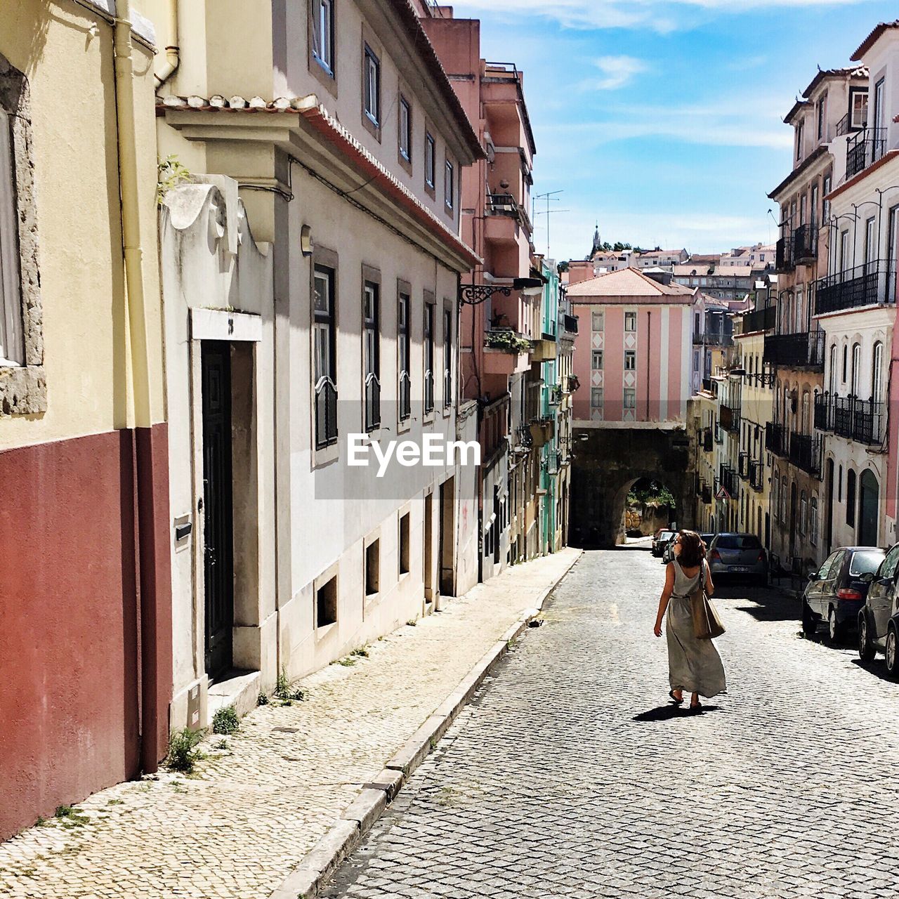 Woman walking on street amidst buildings against sky