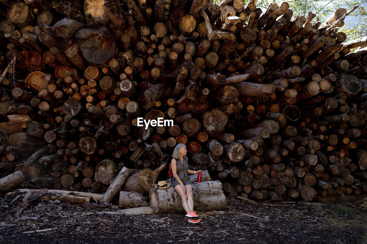 Senior woman sitting on log in front of stack of wood