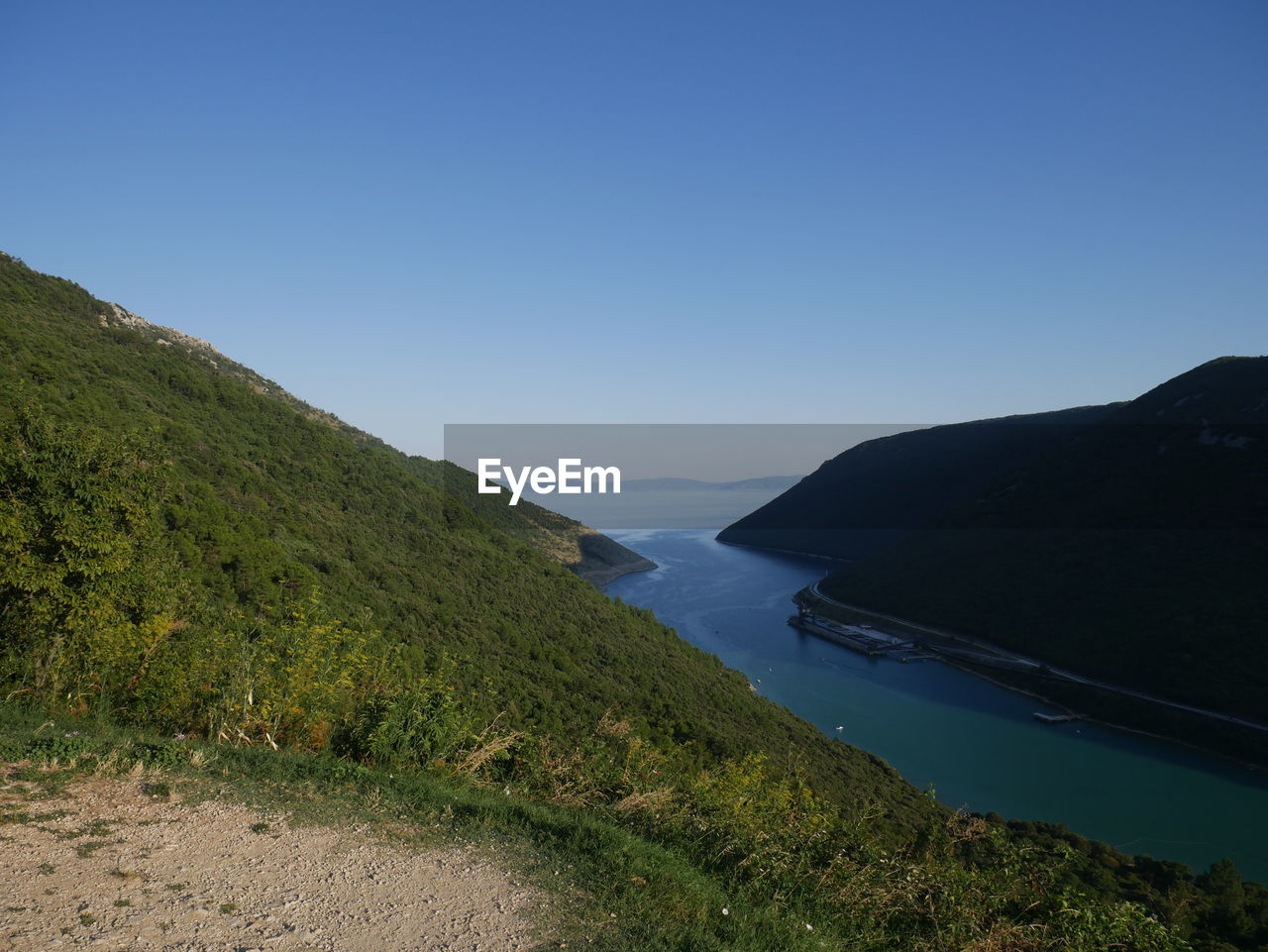 Scenic view of sea and mountains against clear blue sky