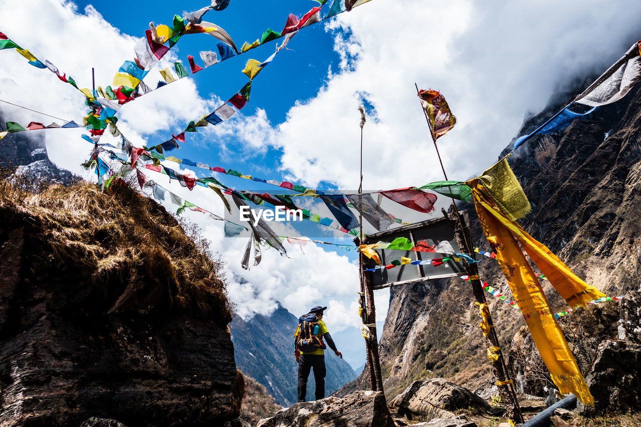 Rear view of man standing on cliff near multi colored flags on mountain against sky