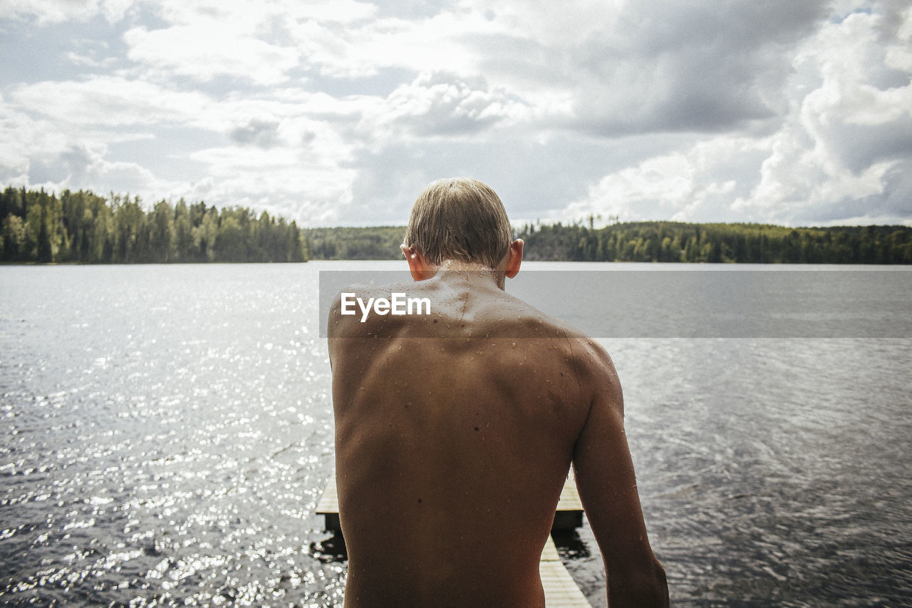 Rear view of shirtless boy standing by lake