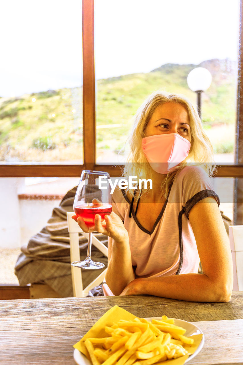Smiling woman wearing mask holding wineglass sitting at restaurant