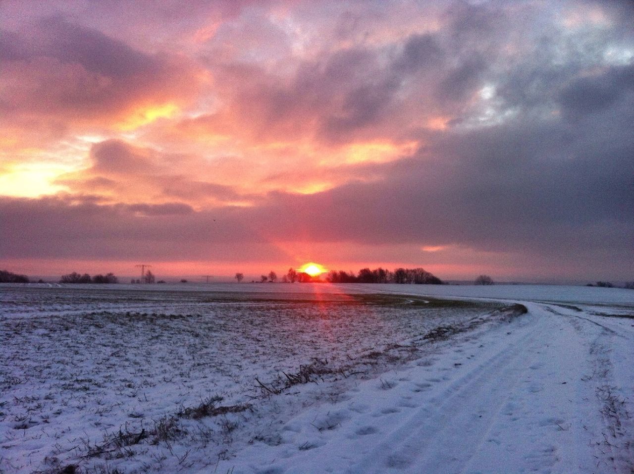 Snow covered country road and landscape against cloudy sky