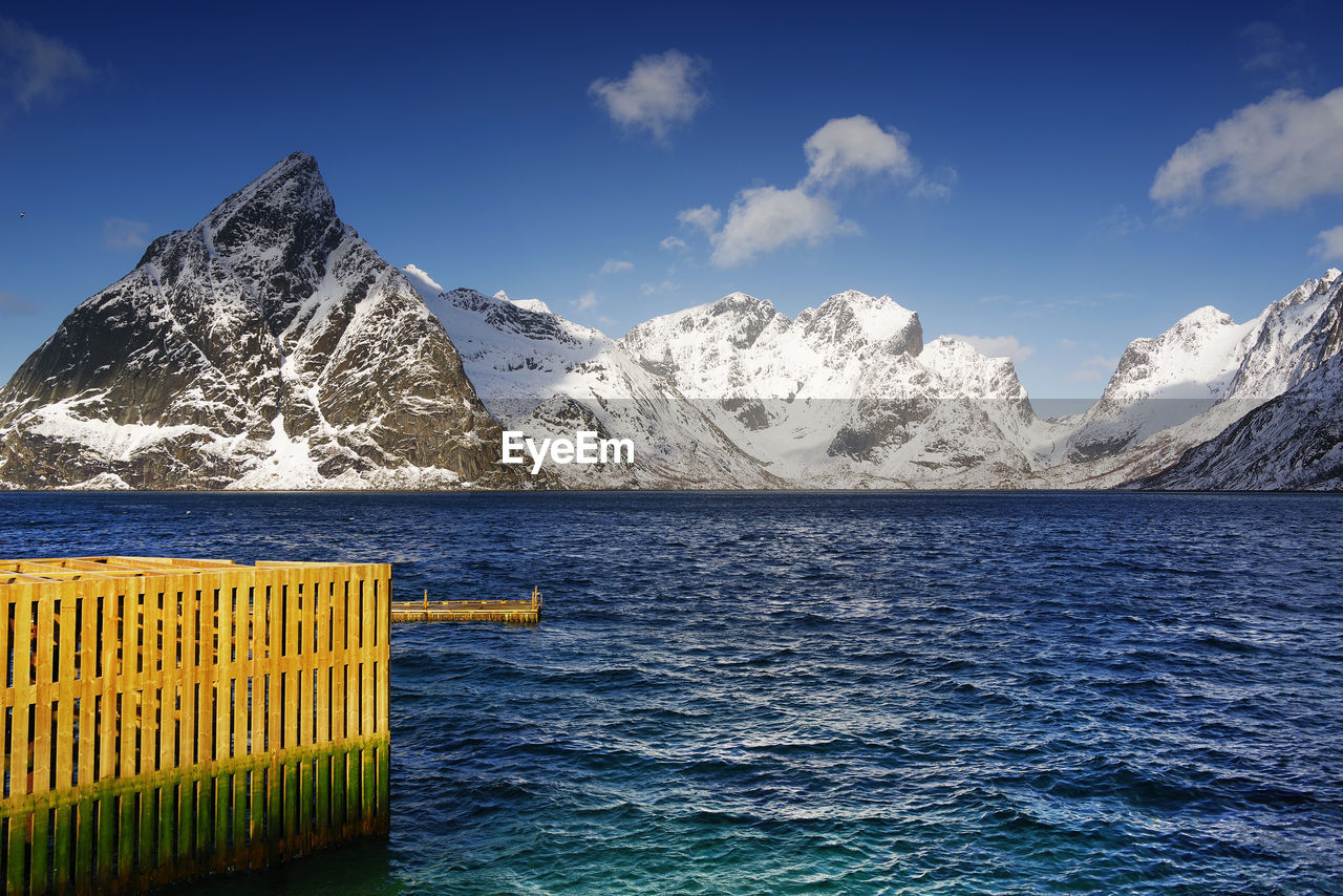 Scenic view of sea by snowcapped mountains against sky