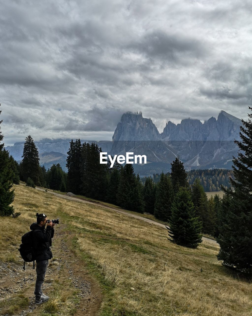 Side view of man photographing on mountain against cloudy sky