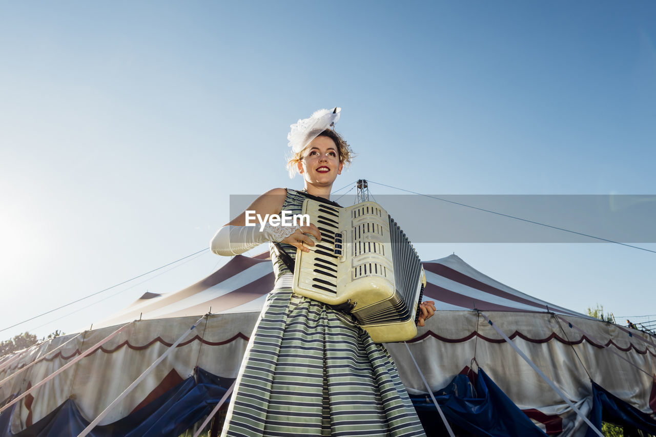 Female performer playing accordion in front of circus tent