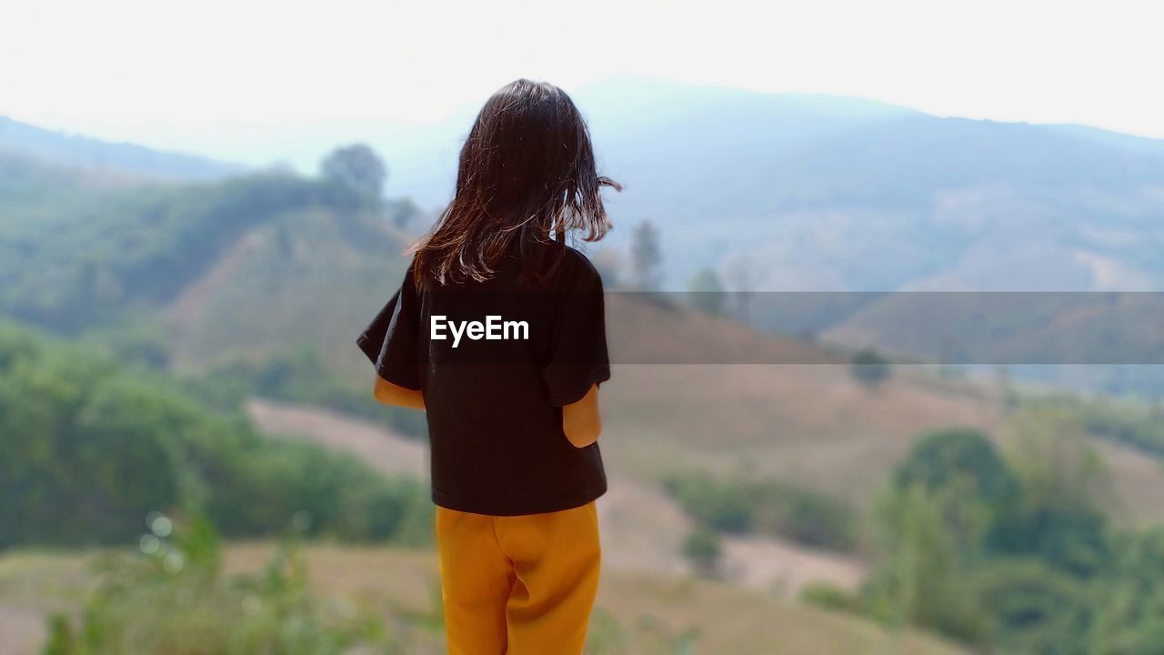 Rear view of teenage girl standing against mountains