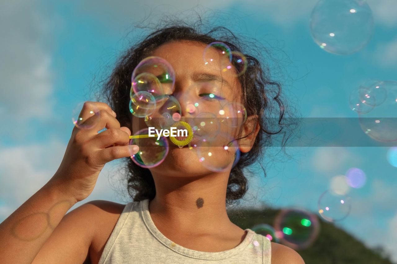 Close-up of girl blowing bubbles against sky