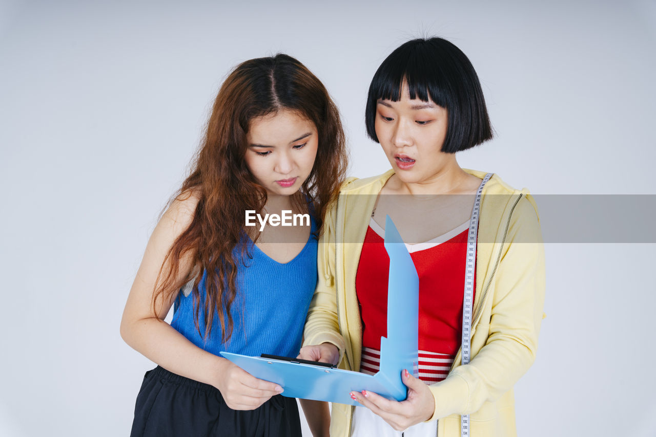 Smiling lesbian couple looking at file against gray background