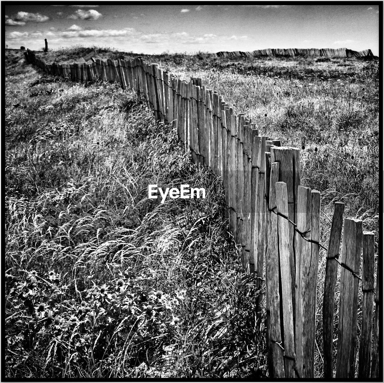 Wooden fence on grassy field against sky