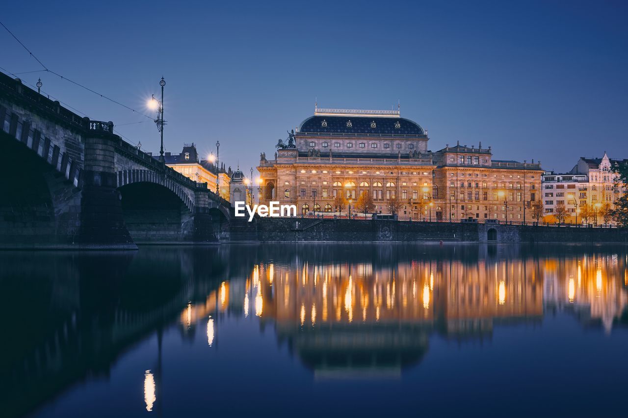 City reflection in vltava river. embankment with national theater at twilight in prague.