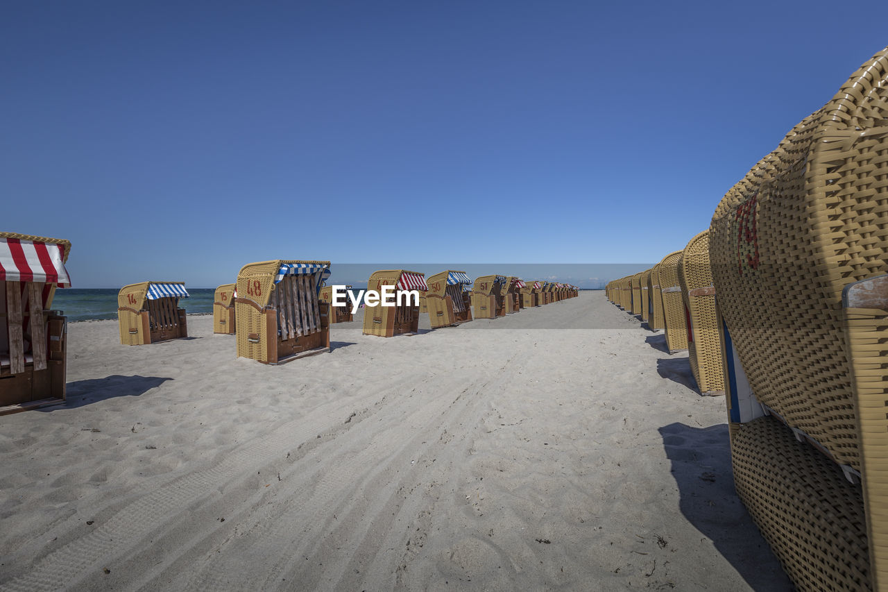 Hooded chairs on beach against clear blue sky