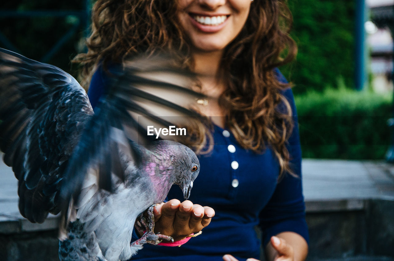 Midsection of smiling woman feeding pigeon