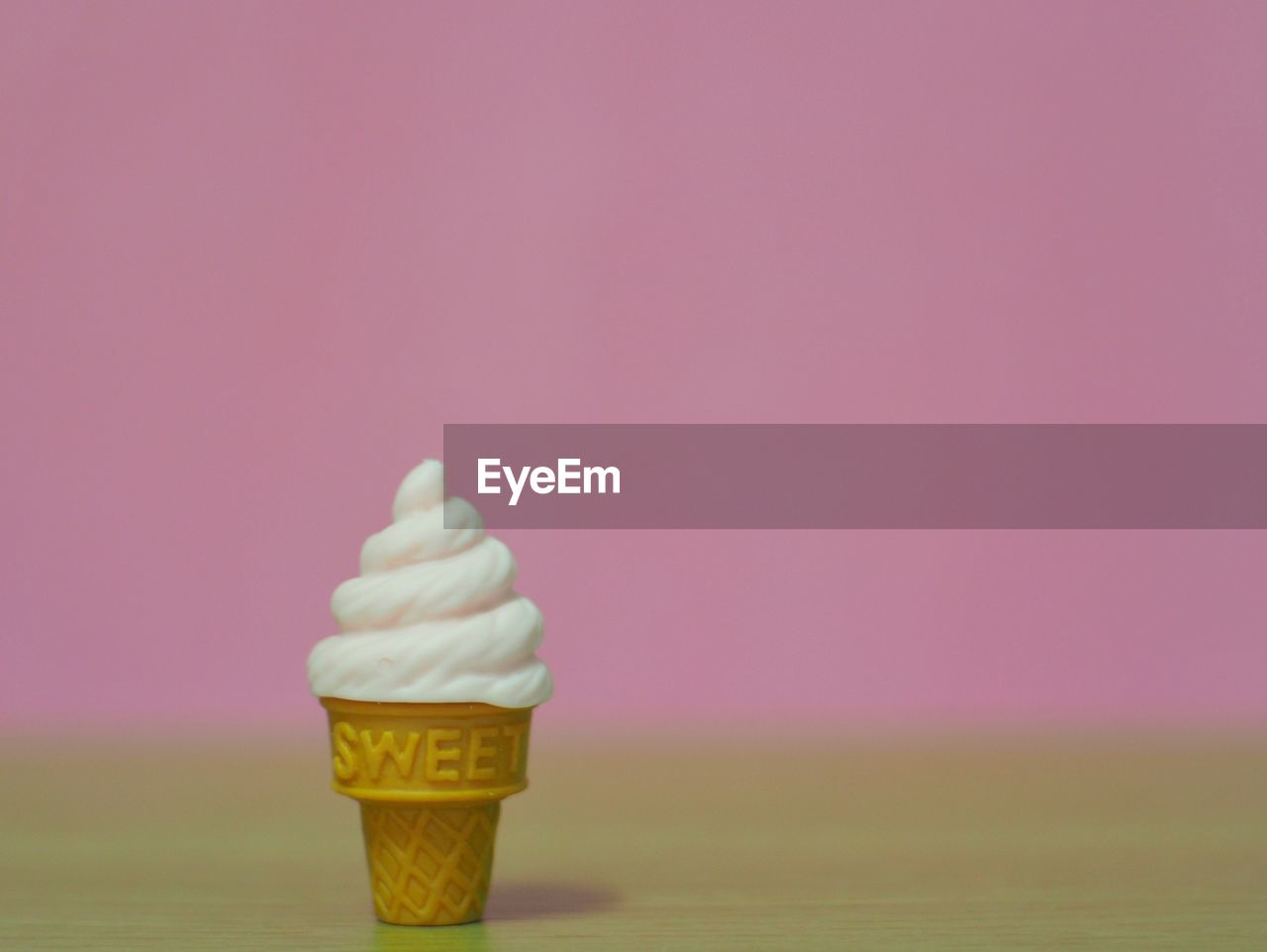 CLOSE-UP OF ICE CREAM CONE ON TABLE AGAINST WALL