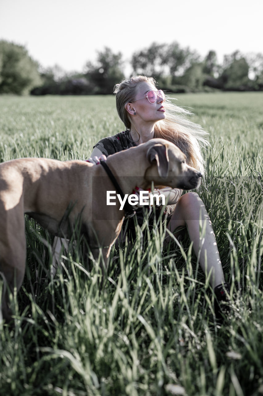 Young woman with dog sitting on grassy field against clear sky