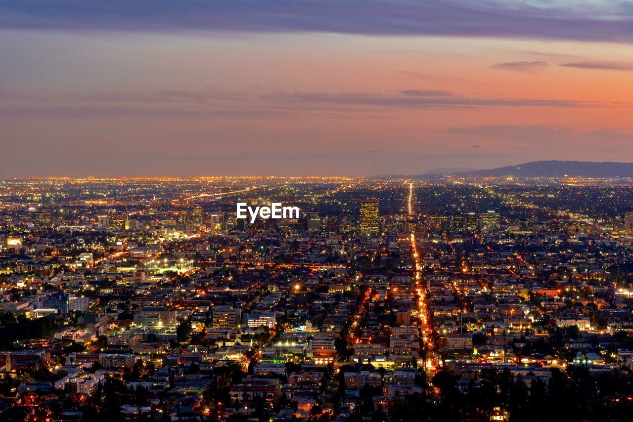 Illuminated cityscape against sky during sunset