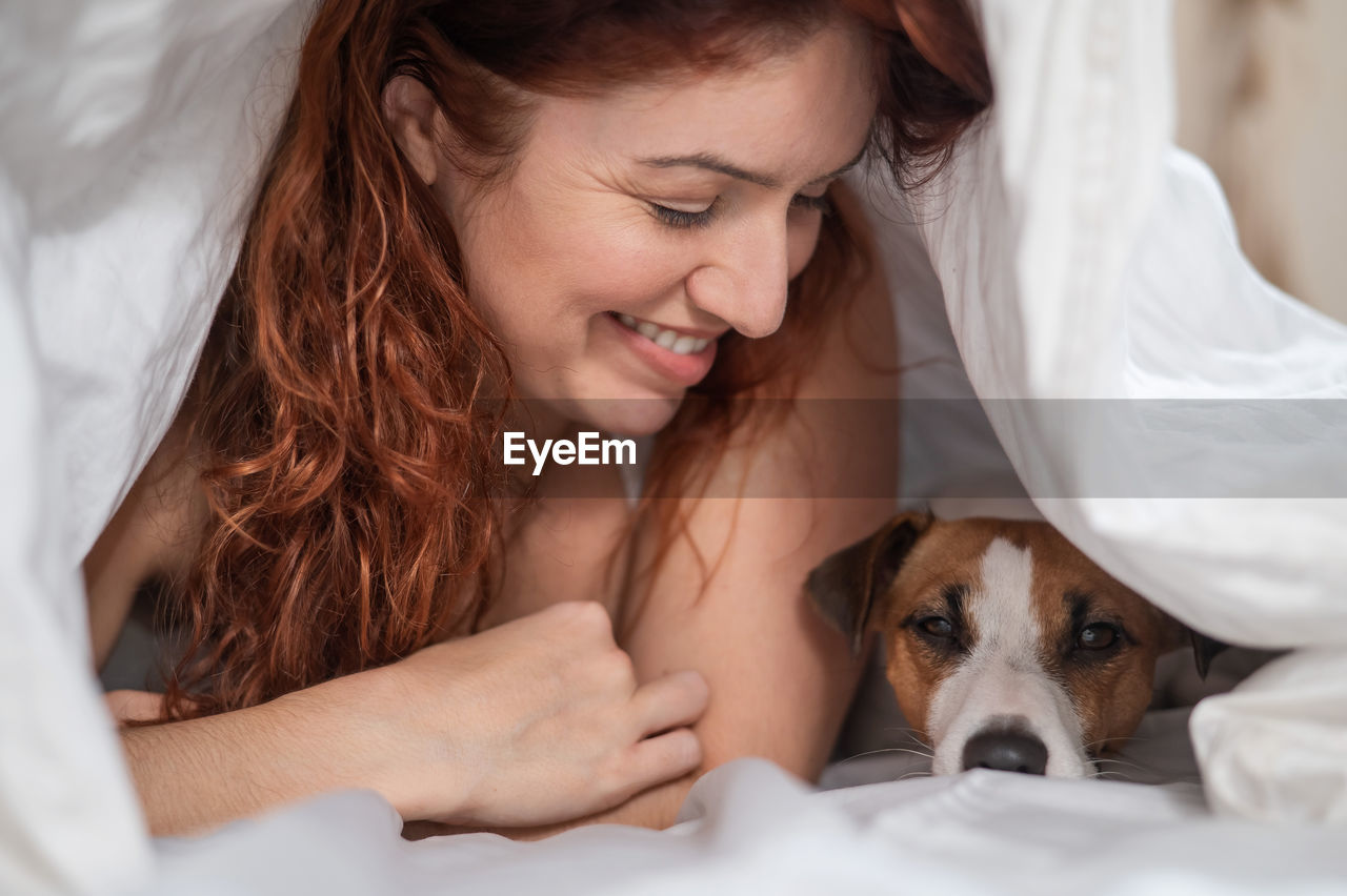 Smiling woman lying on bed with dog
