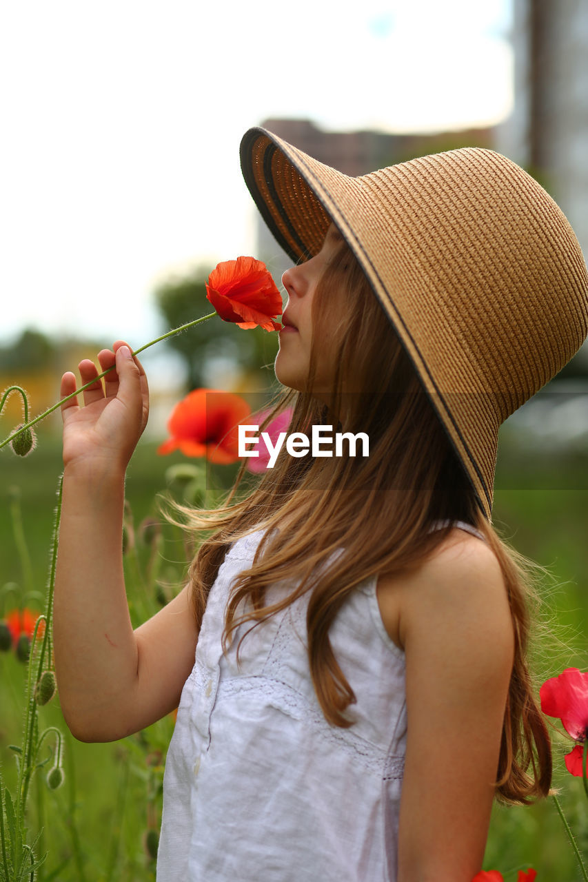 Portrait of a cute girl wearing a straw hat and walking in the poppy field
