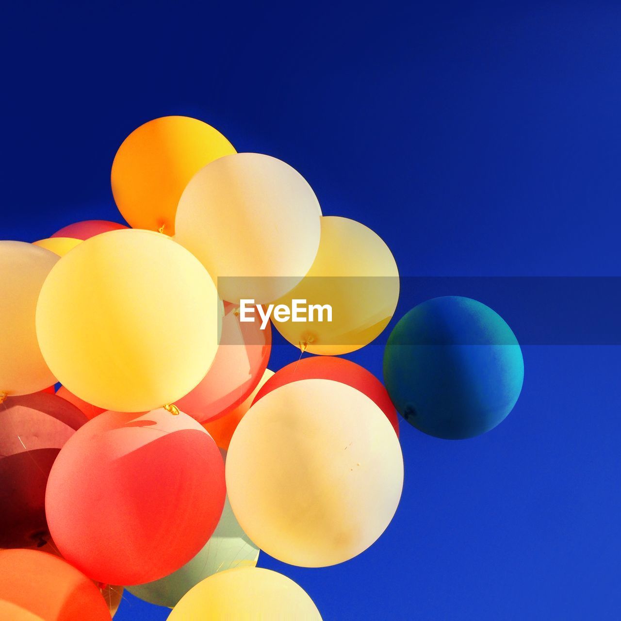 Low angle view of multi colored balloons against clear blue sky on sunny day