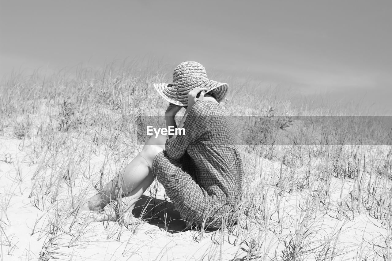 Rear view of woman sitting on field against sky