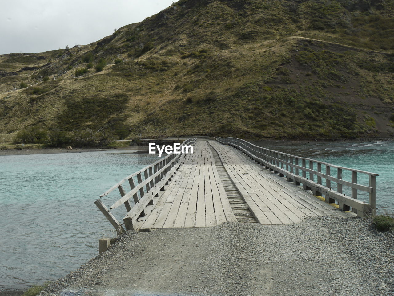 Scenic view of river with woodbridge by mountains against sky