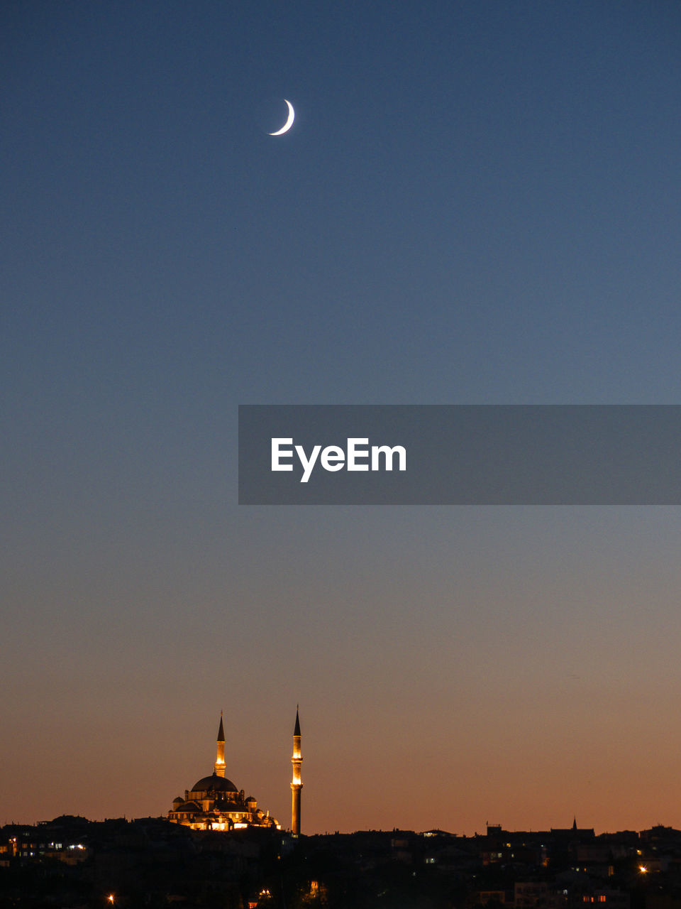 Moon over illuminated mosque against clear sky at night