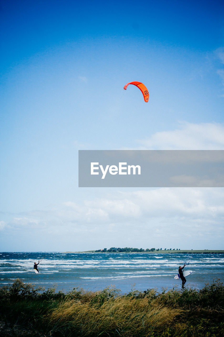 Men kiteboarding on sea against sky