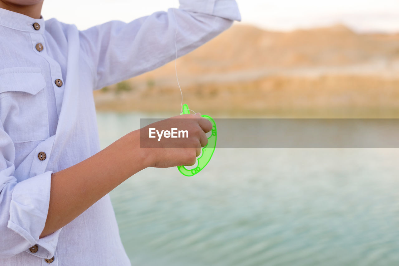 A child's hand holds a fishing line from a kite.