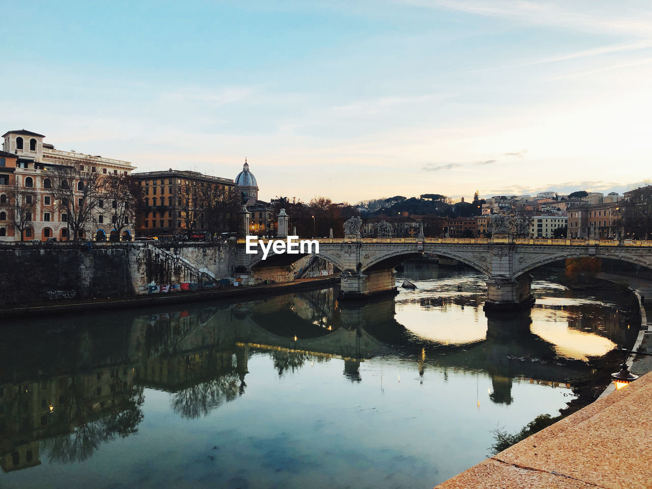 Bridge over river by buildings against sky in city