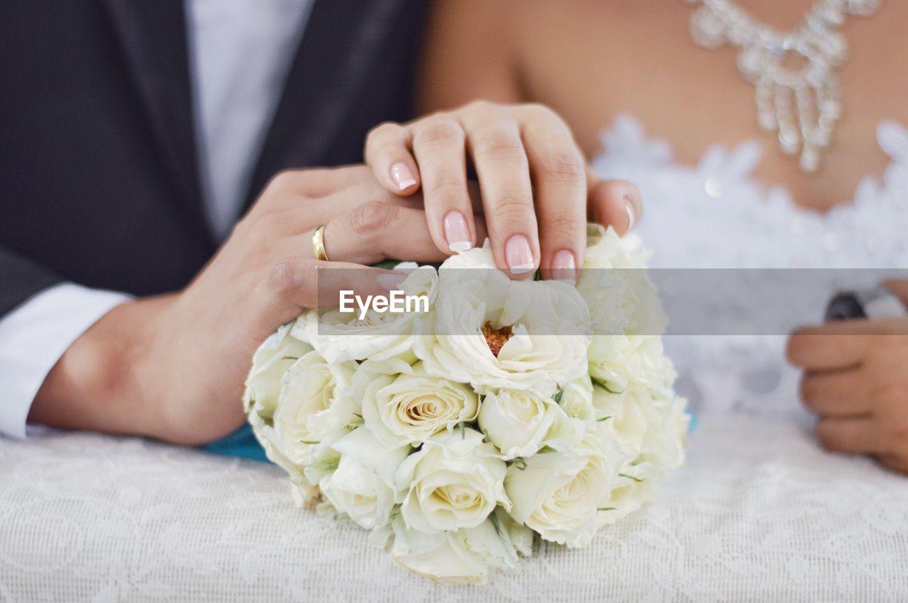 Cropped image of bride and groom touching rose bouquet