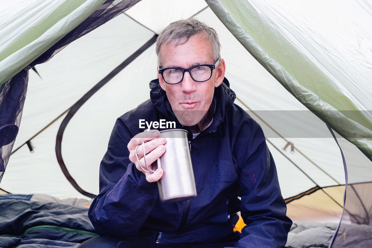 Man in camping tent drinking from tin mug