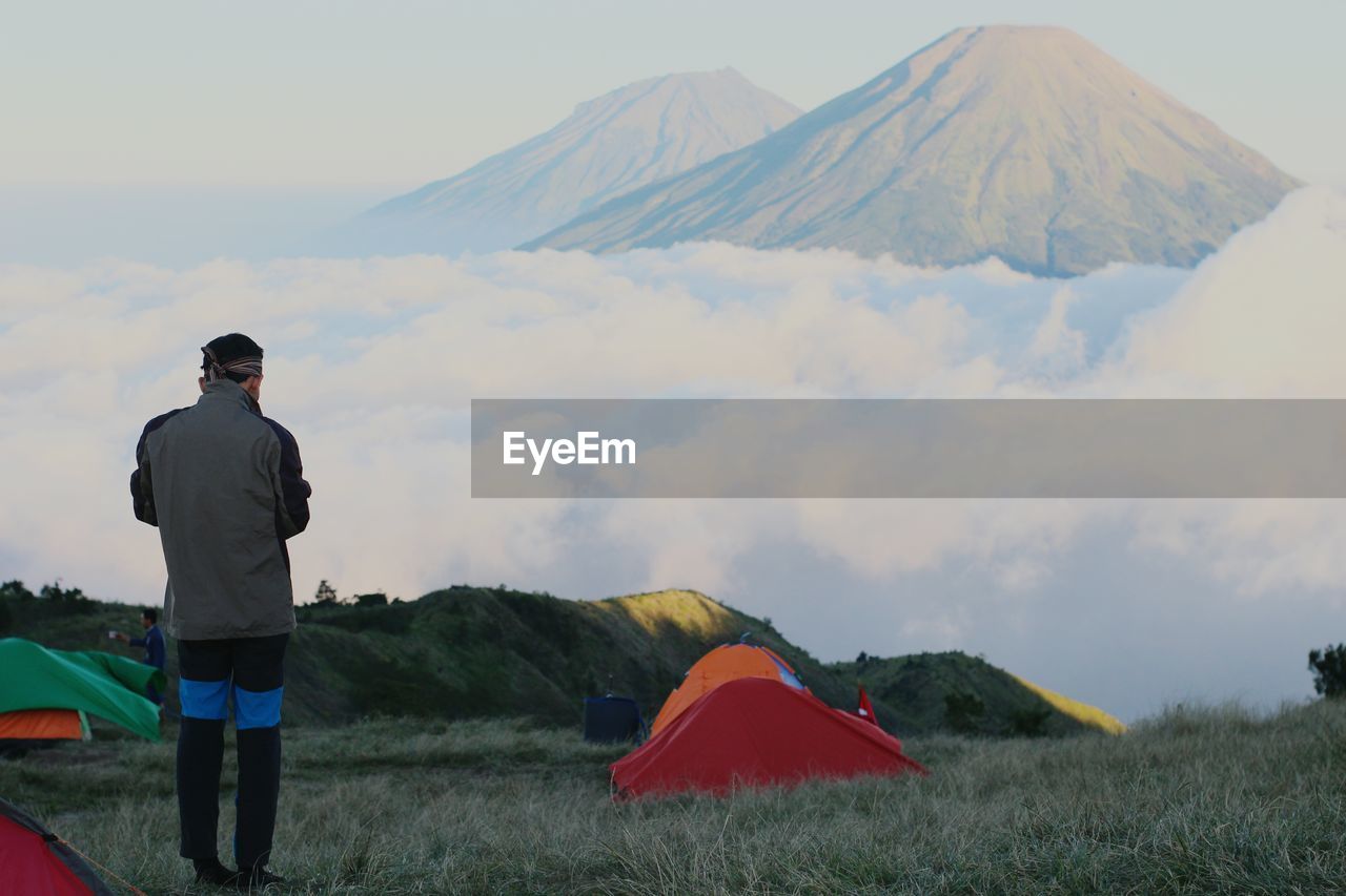 Rear view of man camping against mountains during sunset