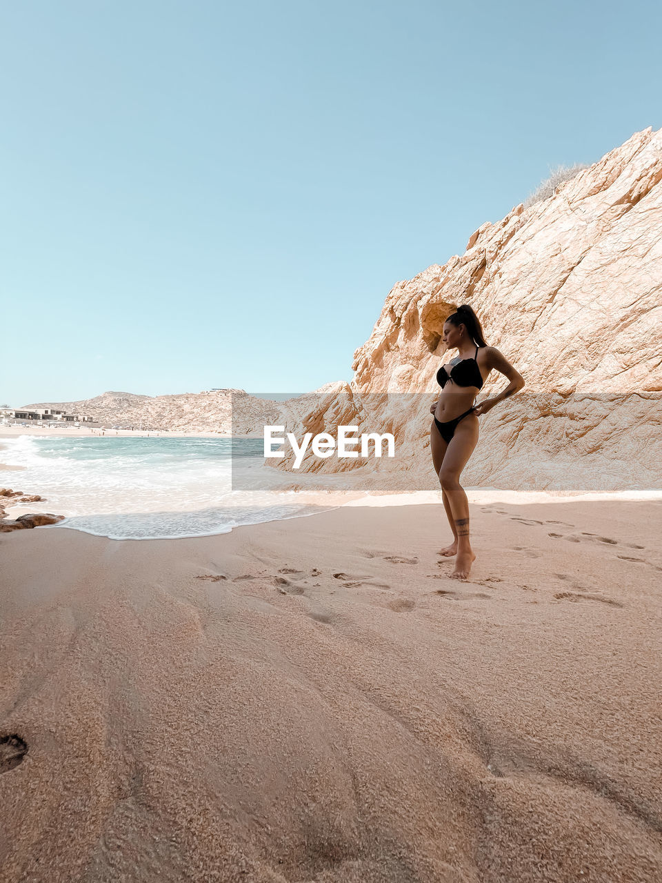 Woman on rock at beach against clear sky