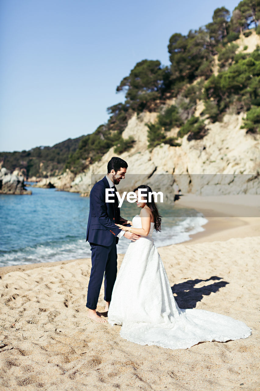 Newlywed couple enjoying at beach against clear sky during sunny day