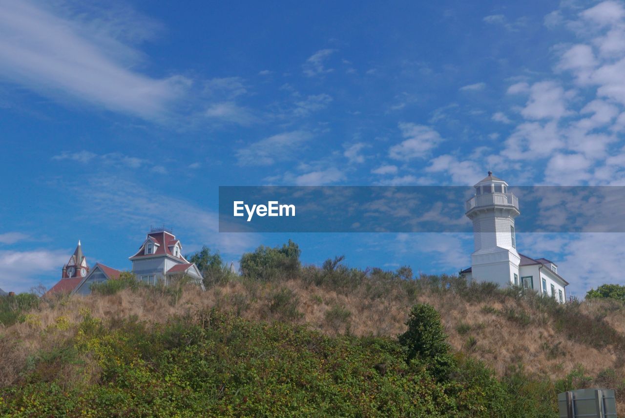 LOW ANGLE VIEW OF LIGHTHOUSE BY BUILDING AGAINST BLUE SKY