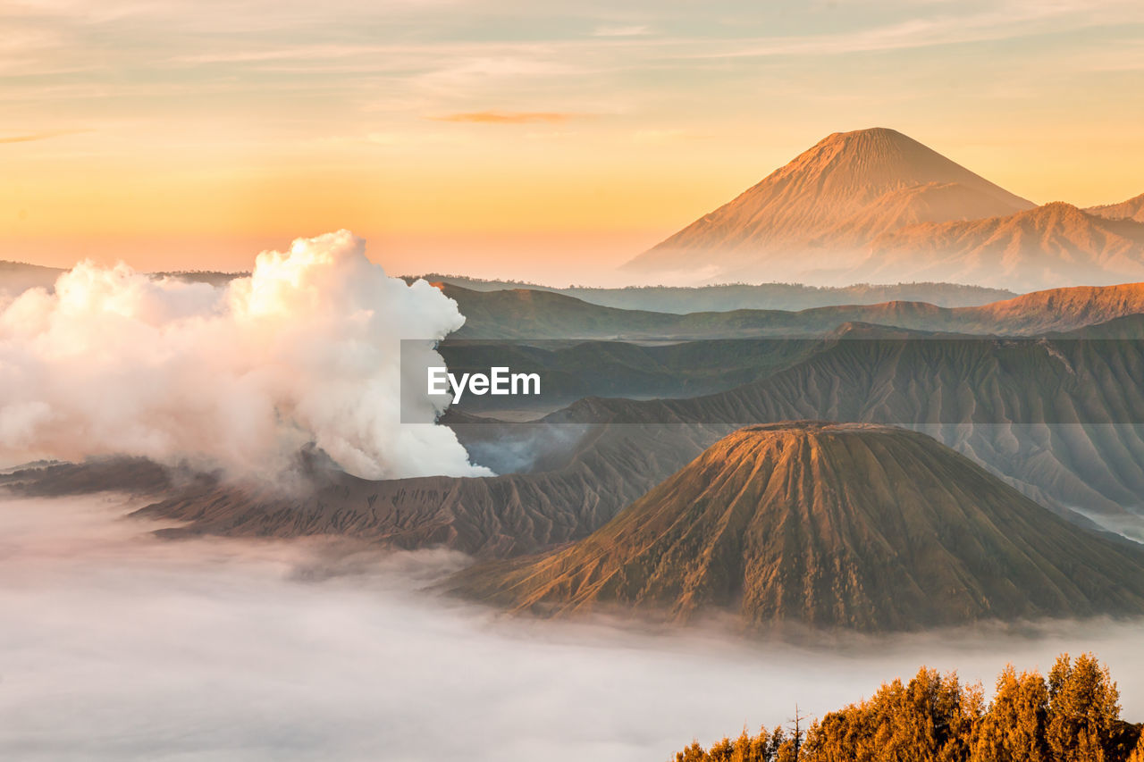 Smoke emitting from volcanic landscape against sky during sunset